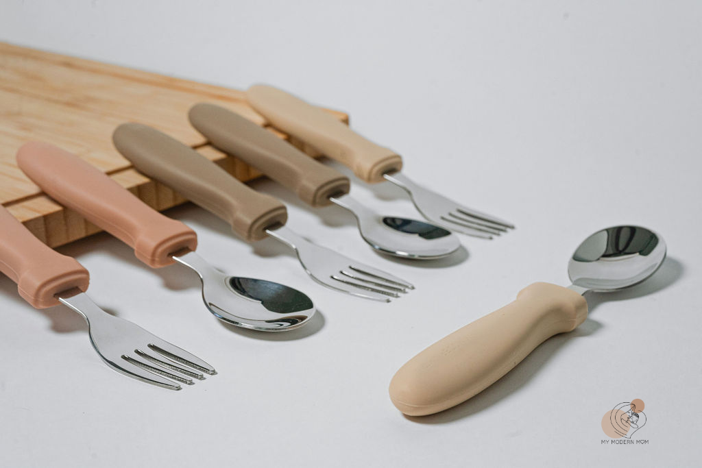 A set of children's cutlery with beige handles laid out on a white surface, including spoons and forks.

